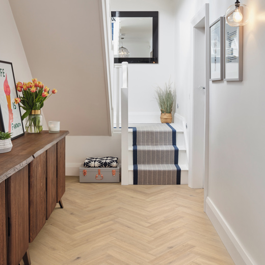 Van Gogh Canadian Nude Oak herringbone mid brown LVT flooring laid in a hallway.